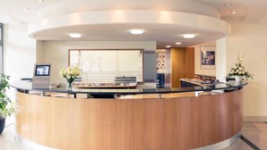 A modern reception desk with a wooden finish, a digital screen, and a vase of flowers.