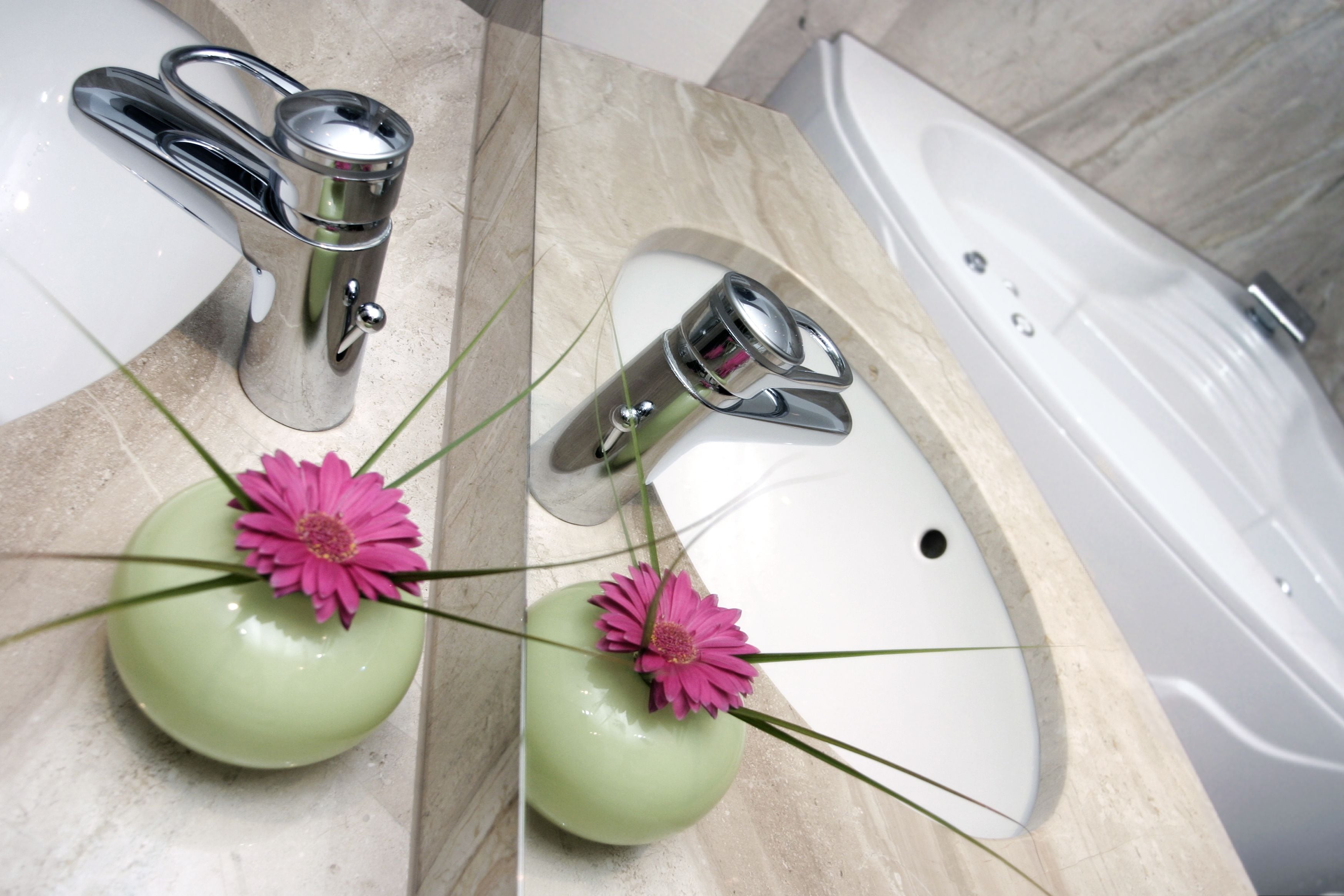 Ein Badezimmer mit weißem Waschbecken, einer grünen Vase mit einer rosa Blume und einer Badewanne.