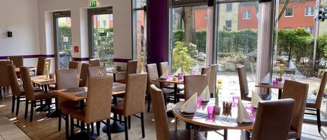 Un restaurante con mesas, sillas, ventanas amplias y vistas al exterior.