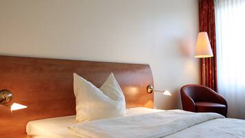 A hotel room with a neatly made bed, a wooden headboard, a red armchair, and two bedside lamps.