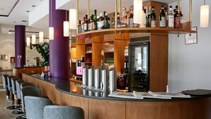 Zona de bar con mostrador curvo, varios taburetes y una variedad de botellas y vasos.
