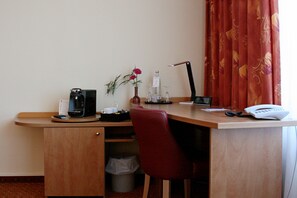 Escritorio de hotel con cafetera, un florero con flores, una lámpara y un teléfono.