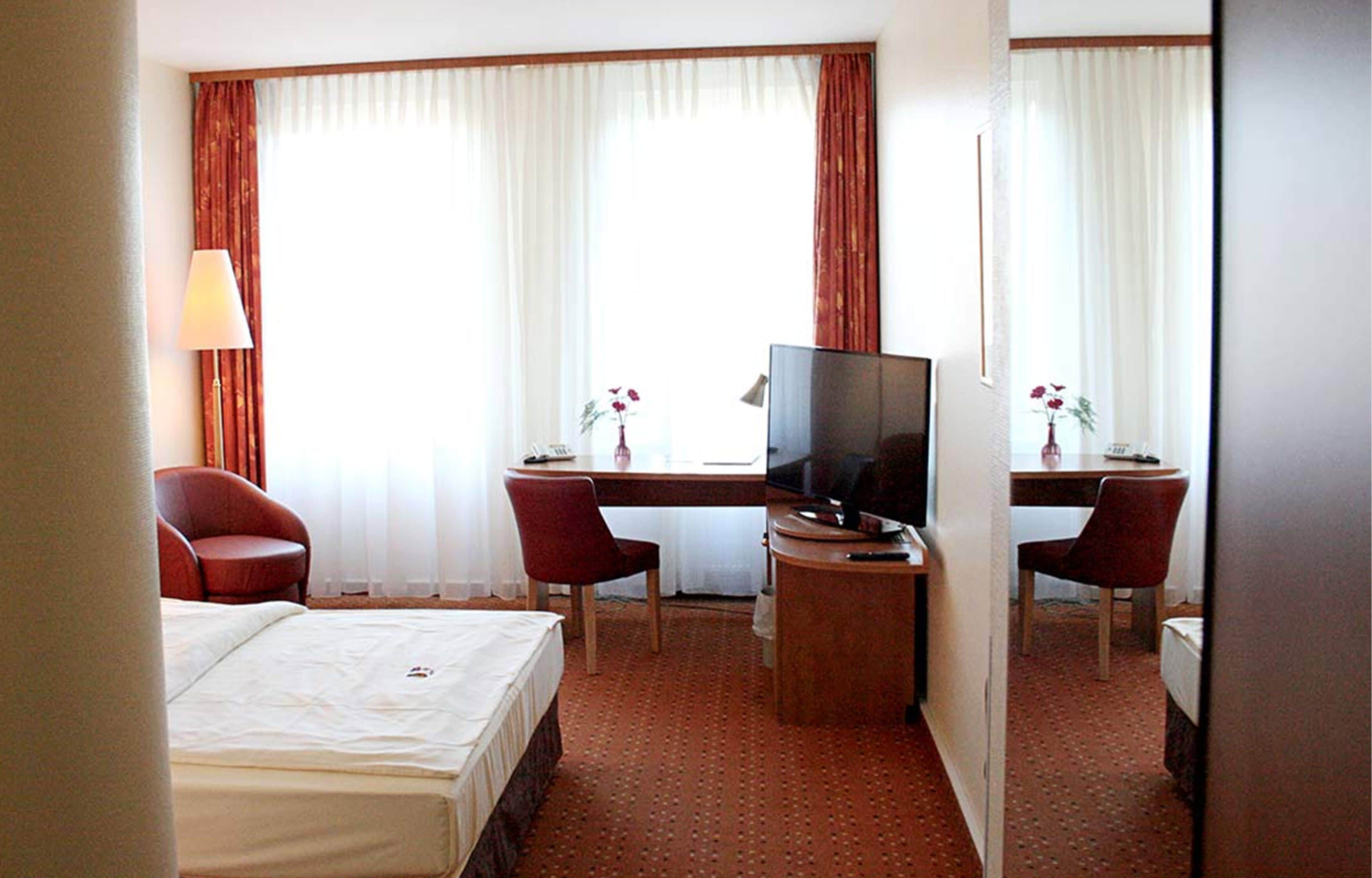 Ein Hotelzimmer mit einem Bett, einem Schreibtisch mit Fernseher, zwei Stühlen und einem kleinen Tisch.