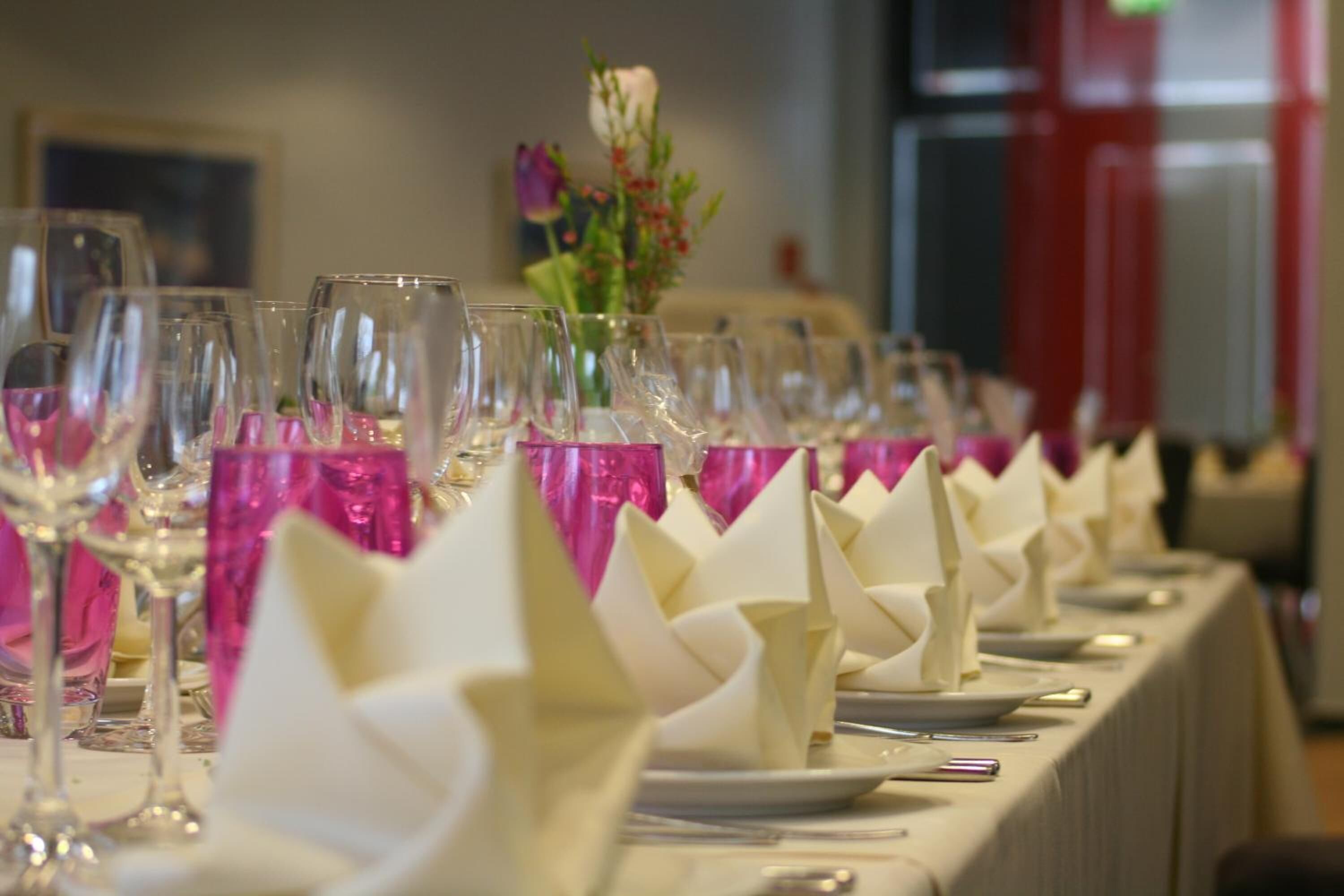 Een lange tafel gedekt met verschillende wijnglazen en opgevouwen servetten, wat wijst op een formele eettafel.