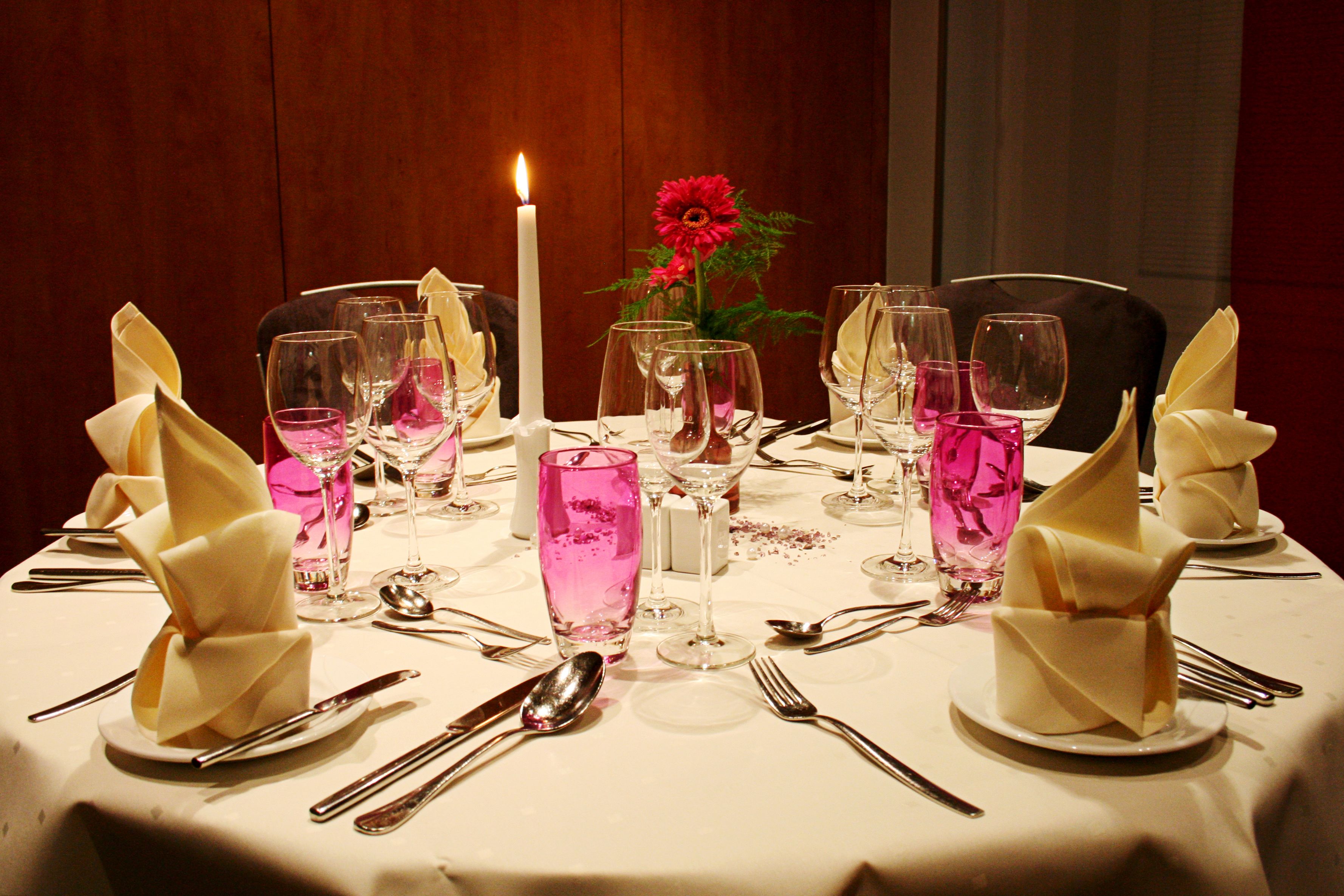 Mesa dispuesta para una cena formal, con una vela encendida, copas rosas y servilletas blancas.