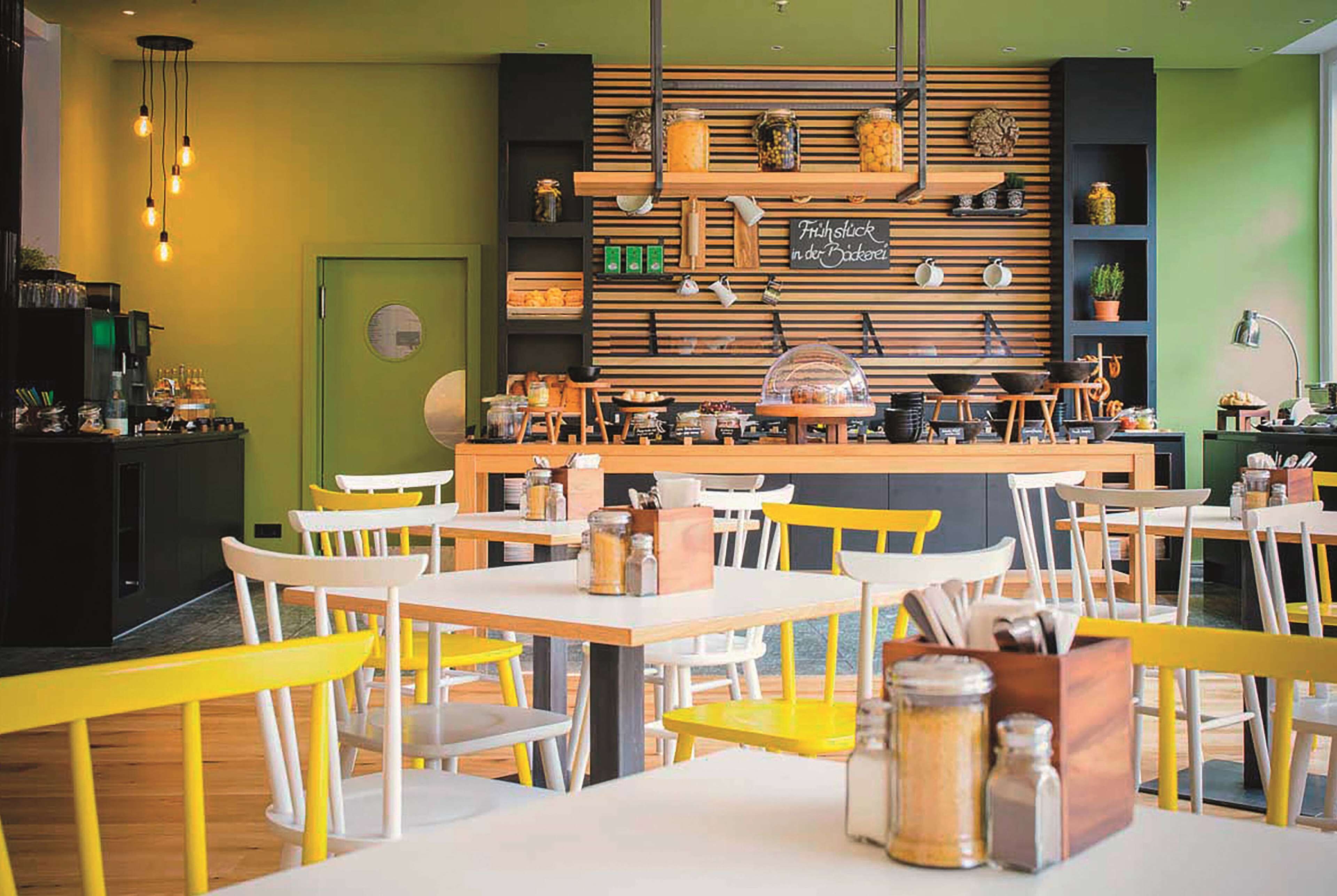 A restaurant interior with wooden shelves, yellow and white chairs, and a counter with various food items.