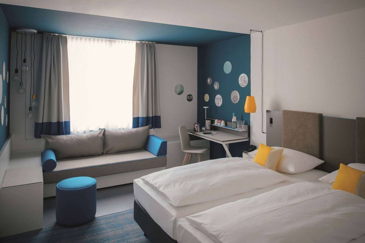 A hotel room with a bed, a desk, a chair, a sofa, and a small ottoman.