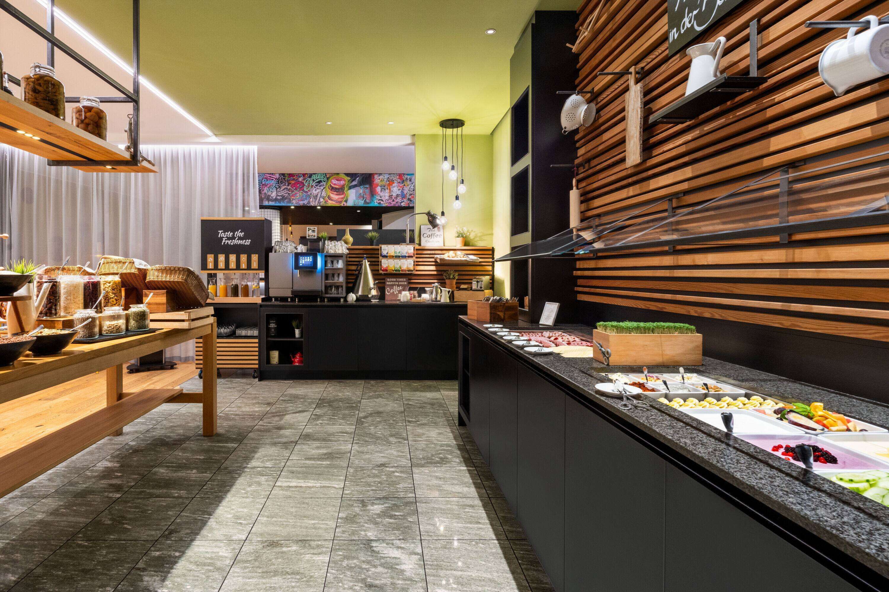 A modern cafe with a buffet-style breakfast bar, a coffee station, and a counter with various food items.
