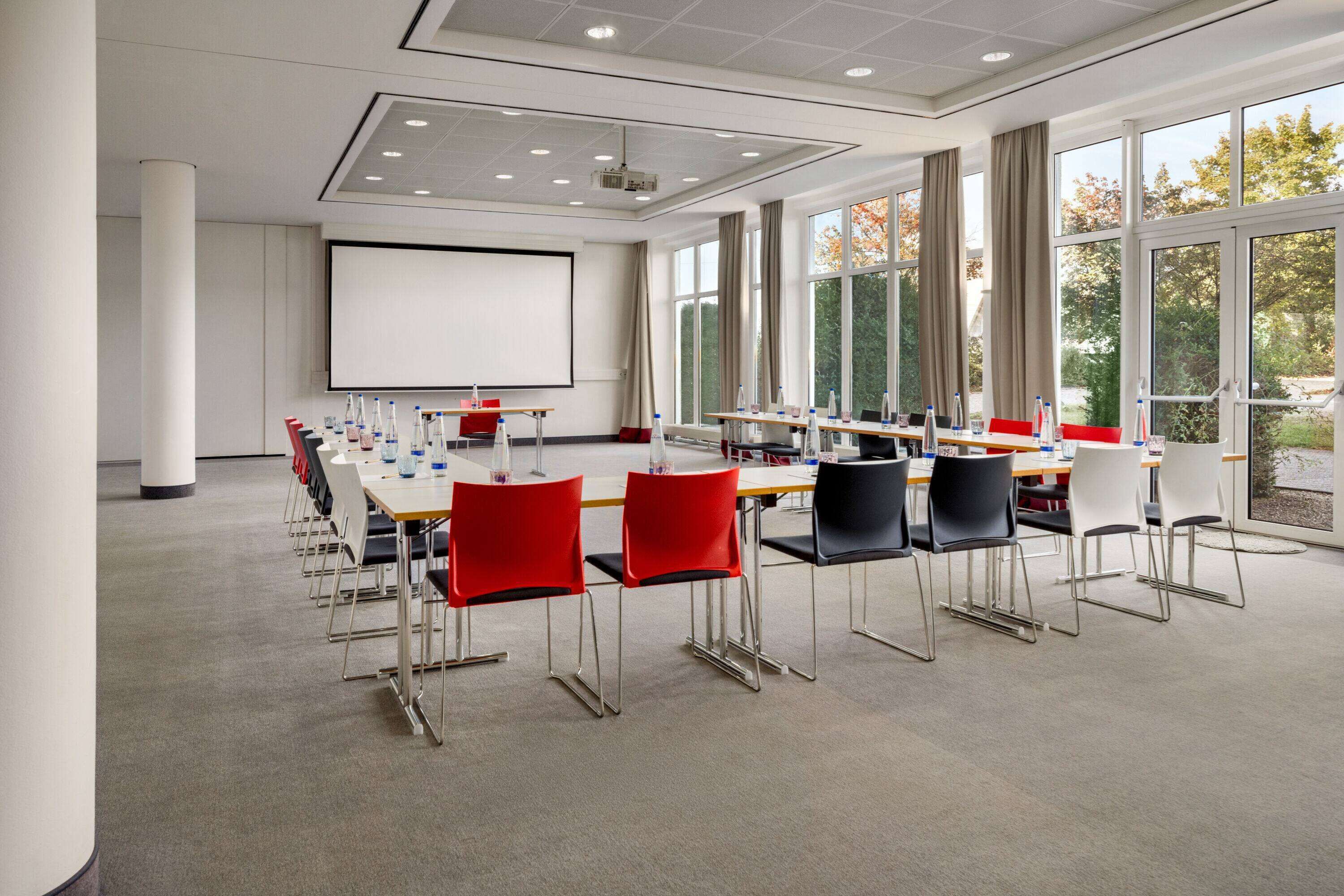 Un salón de conferencias con una pantalla grande, varias mesas y sillas.