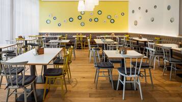 Un grand espace dédié à la salle à manger, avec plusieurs tables et chaises, un mur d’accent jaune orné d’assiettes décoratives et un plancher en bois.