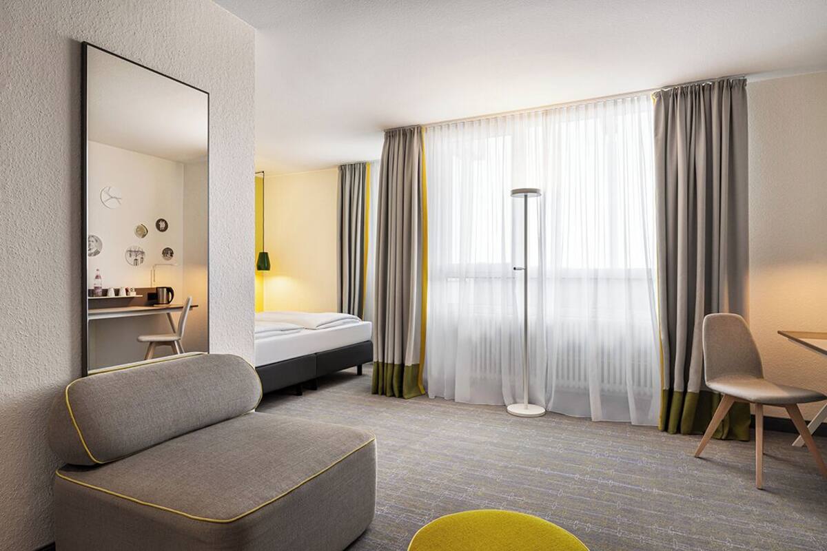 A modern hotel room with a bed, a sofa, a desk, and a chair.