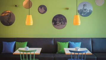 A modern interior with a green wall, two black sofas, and two white tables with blue chairs.