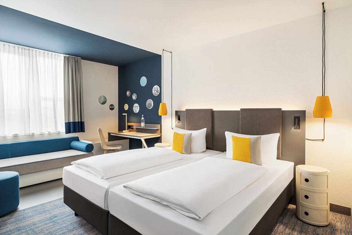A hotel room with two beds, a desk, a chair, a small table, and a sofa.