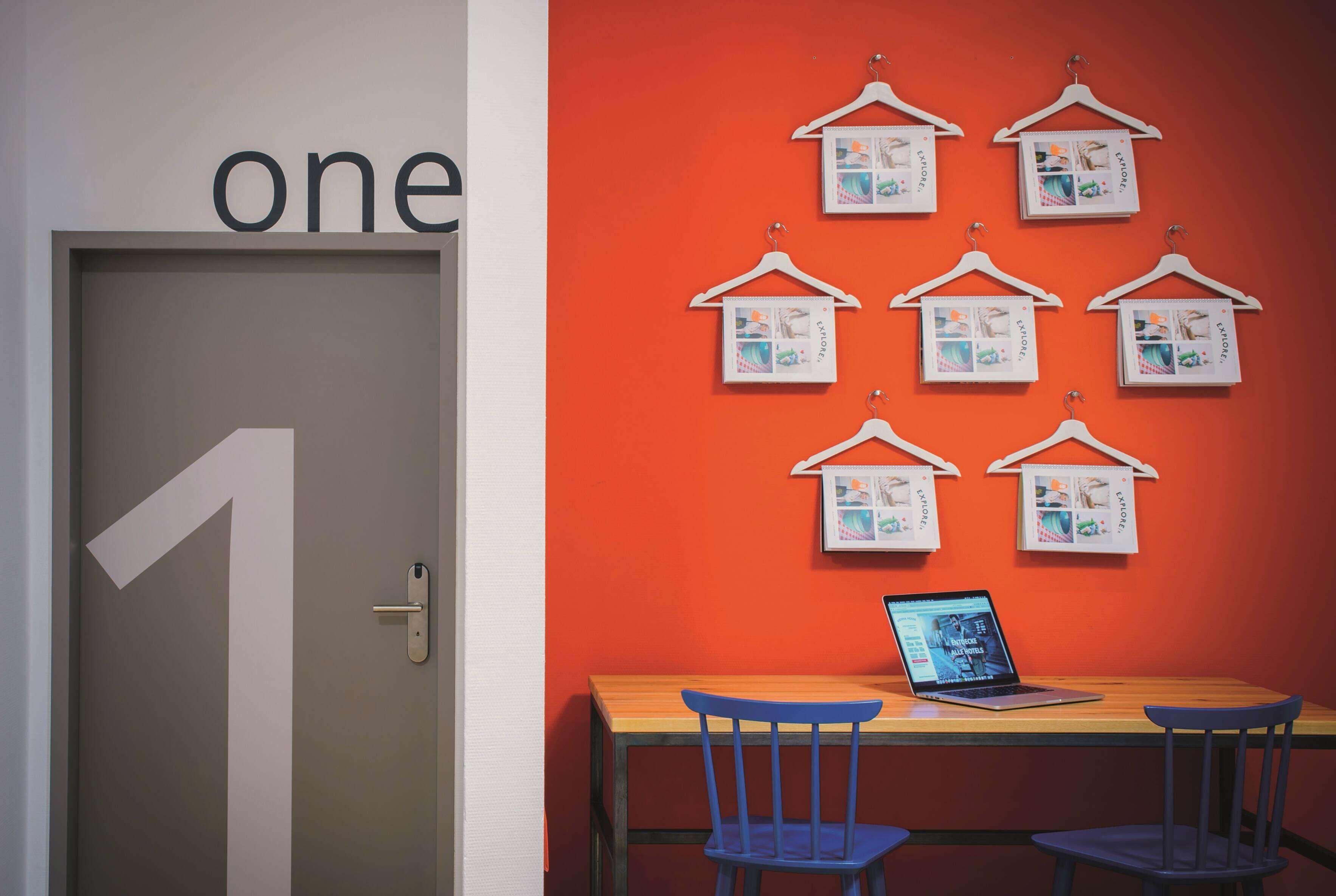 A room with a door labeled 'one', a wooden table with a laptop, and a wall decorated with hanging pictures.