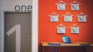A room with a door labeled 'one', a wooden table with a laptop, and a wall decorated with hanging pictures.