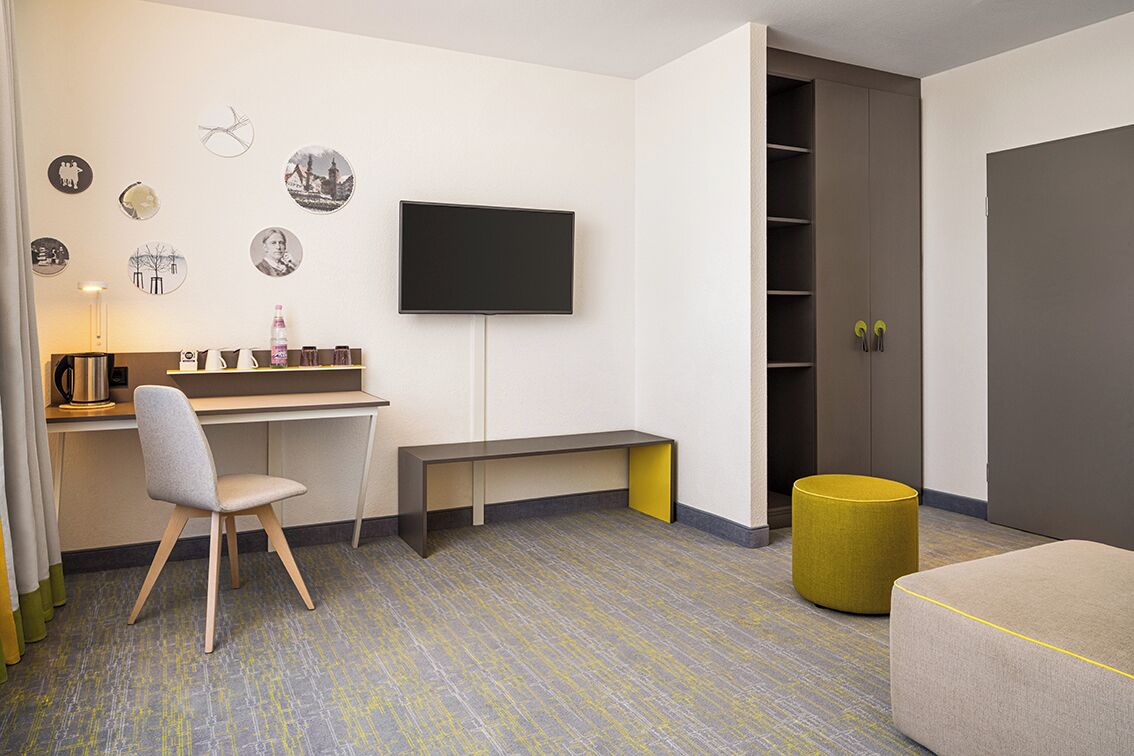 Een moderne kamer met een bureau, stoel, televisie, garderobe en poef.