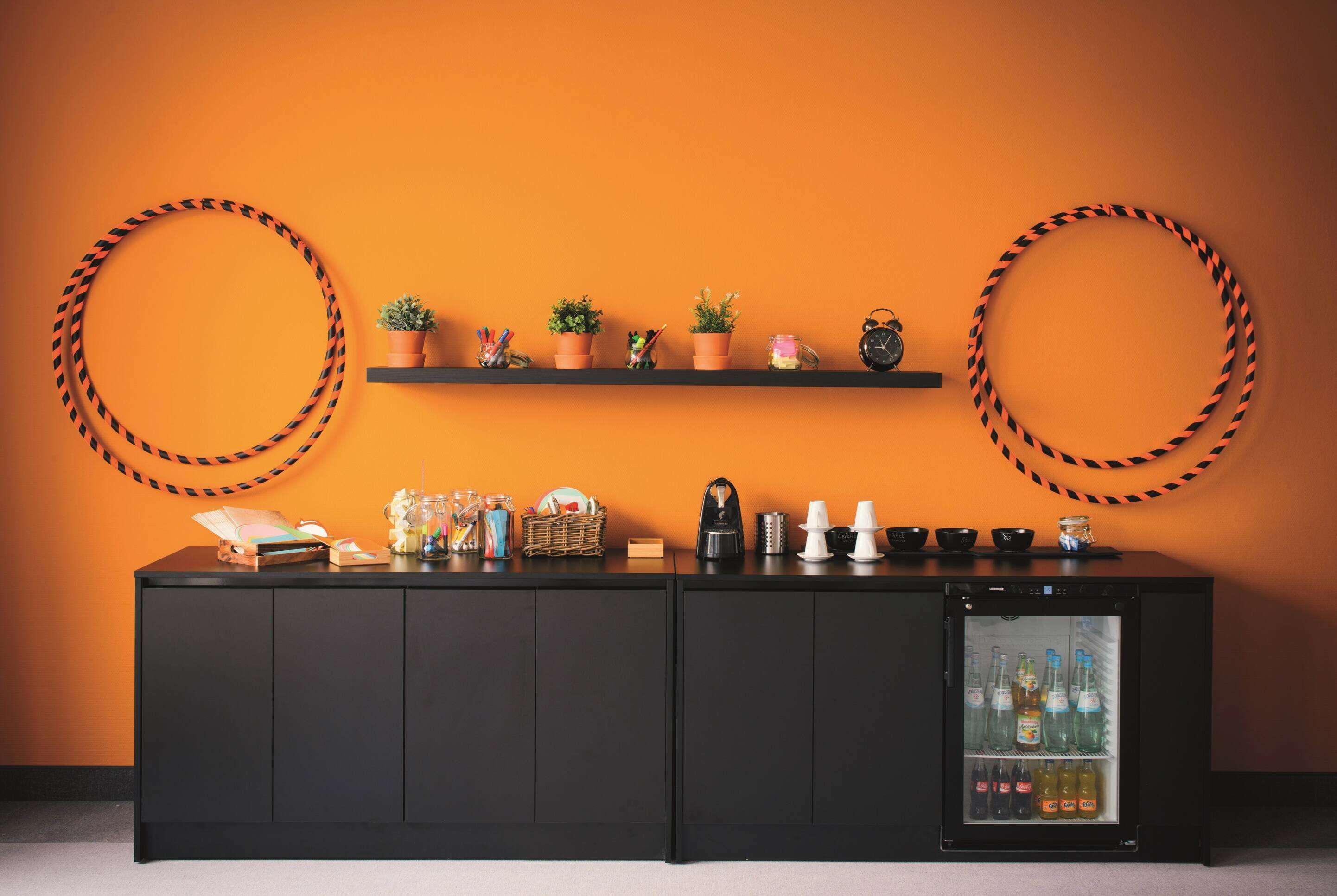 A bar area with a black cabinet, shelves with plants, and a mini-fridge with beverages.