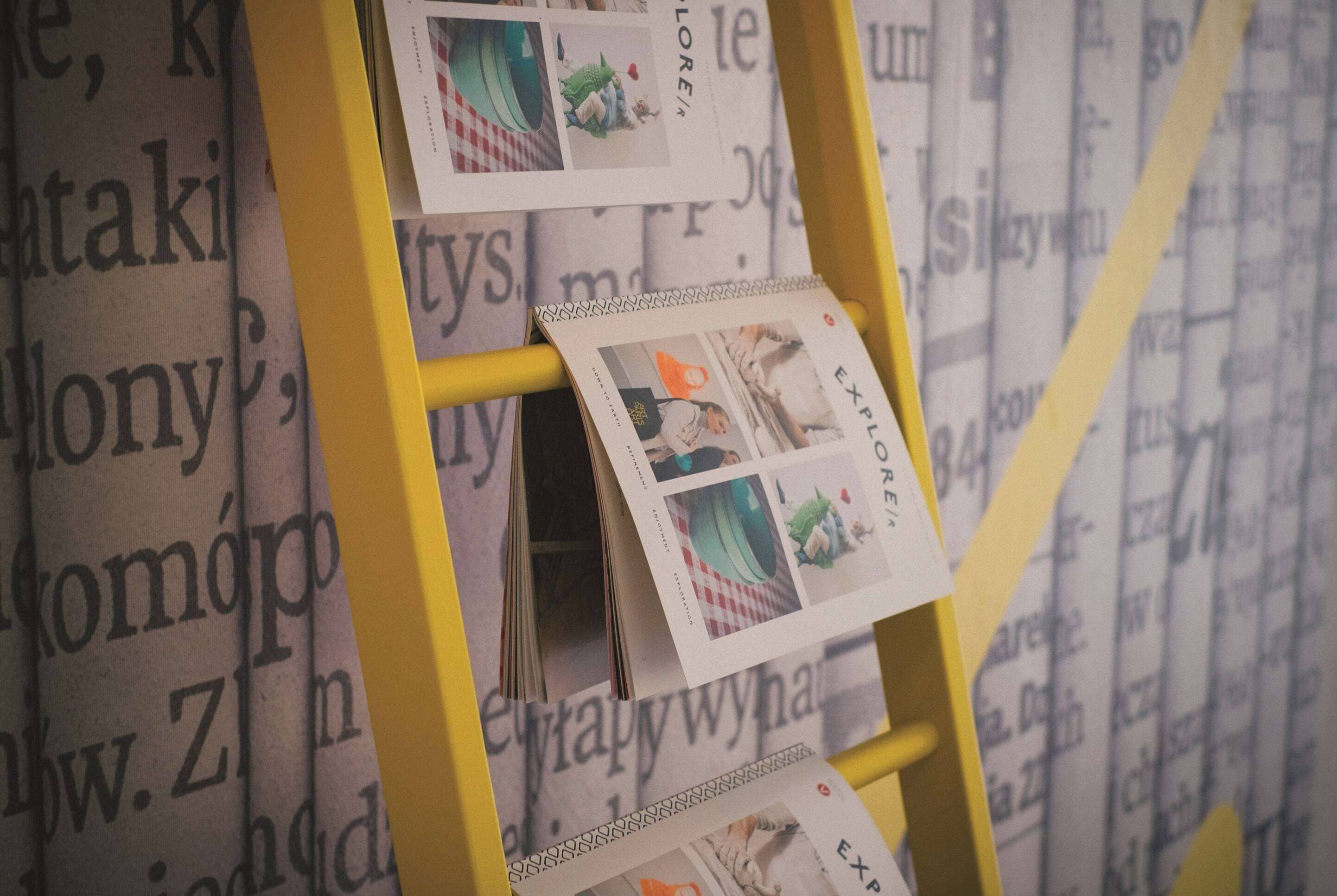 Una escalera amarilla con fotografías sujetas a ella, apoyada en una pared con texto impreso.
