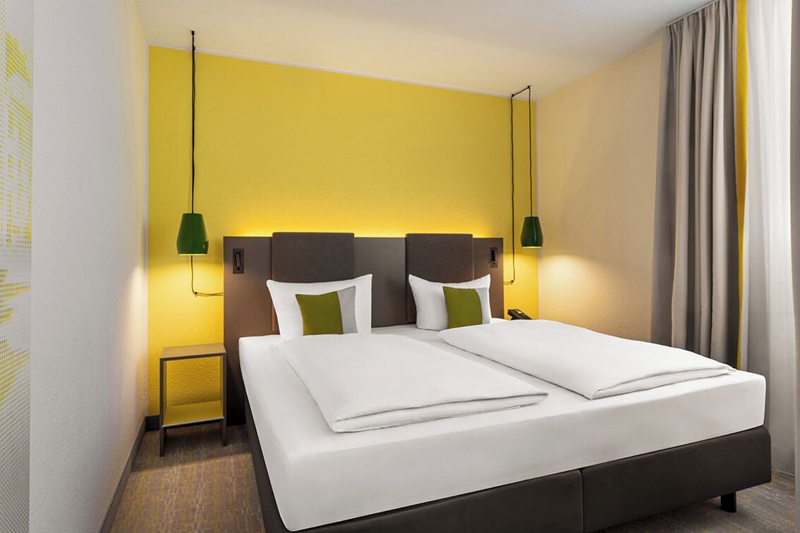 Une chambre d’hôtel avec un grand lit, deux tables de chevet et une petite table de nuit.