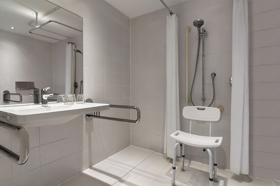 Un baño moderno con ducha, lavabo con baranda y una silla blanca.