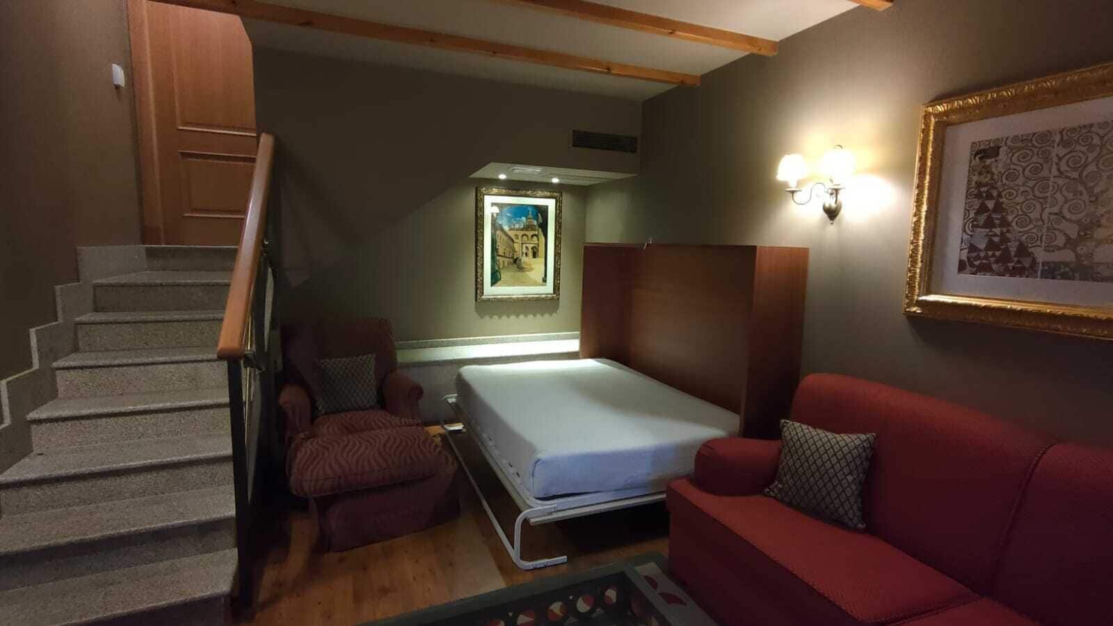Una stanza compatta con un letto, un divano rosso, una sedia e una scala.
