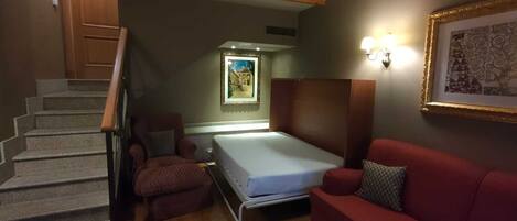 Una habitación compacta con una cama, un sofá rojo, una silla y una escalera.