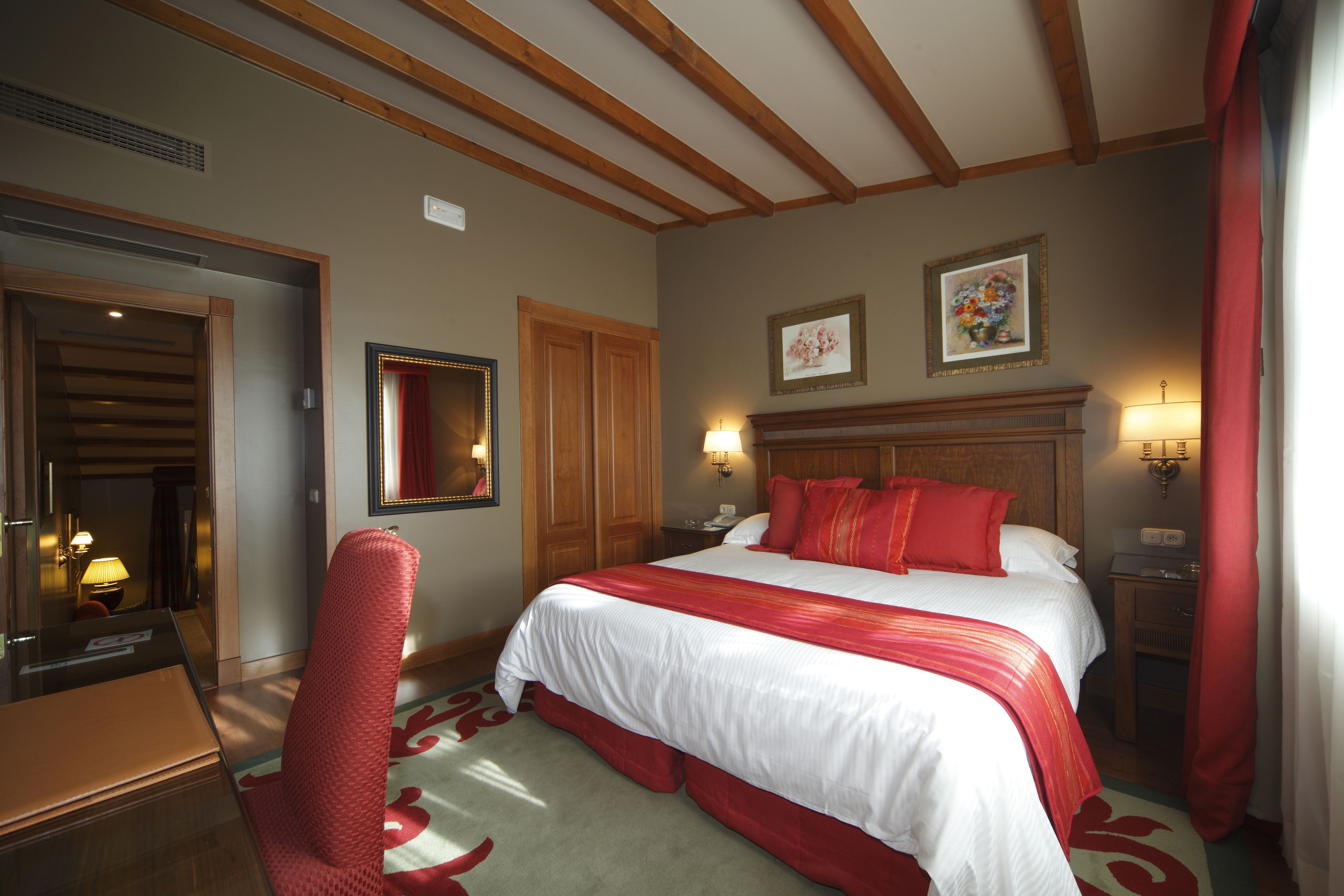 Een hotelkamer met een groot bed, een houten hoofdeinde, een bureau met stoel en een spiegel.