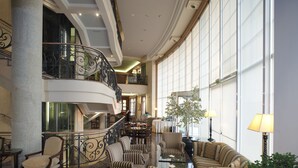 Un hall d’entrée spacieux avec un grand escalier, des sièges confortables et de grandes fenêtres.
