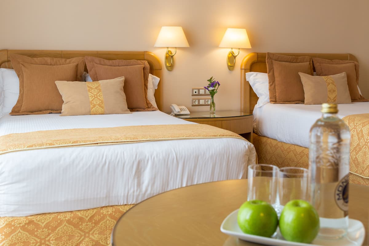 Een hotelkamer met twee bedden, een nachtkastje met een lamp, een telefoon en een dienblad met appels en een fles.
