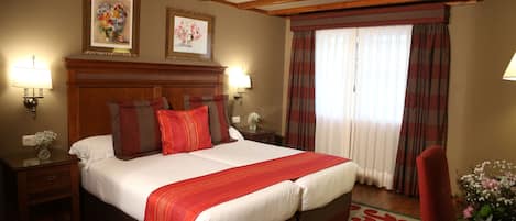 Ein Hotelzimmer mit einem großen Bett, einem Holz-Kopfteil, zwei Nachttischen mit Lampen, einer rot-weiß gestreiften Tagesdecke, einem roten Sessel, einem kleinen Tisch mit Blumenvase und zwei gerahmten Bildern an der Wand.