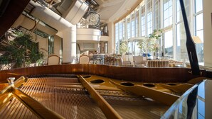 Un piano à queue dans une pièce spacieuse, dotée de grandes fenêtres, d’un mobilier élégant et d’un plafond haut avec des puits de lumière.