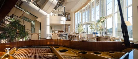 Un piano de cola en una habitación amplia con ventanas grandes, muebles elegantes y un techo alto con tragaluces.