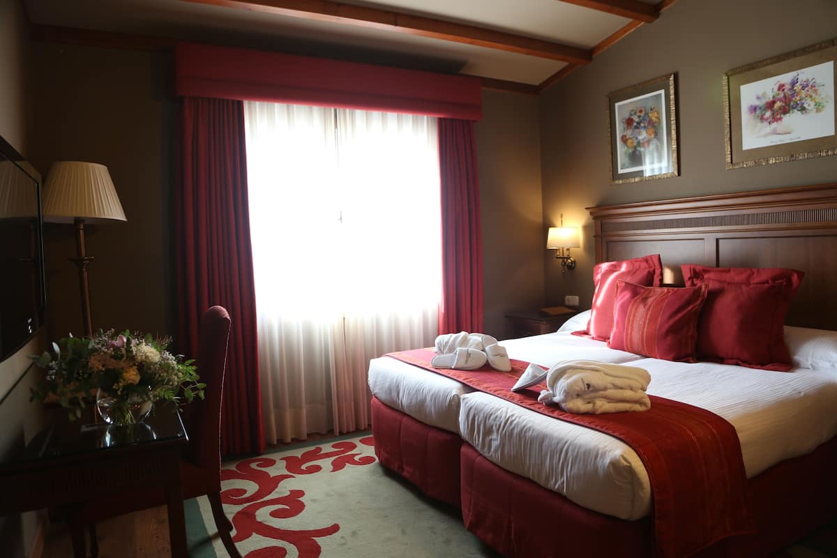 Een hotelkamer met een groot bed, rode beddengoed, een bureau met een lamp en een bloemenvaas.