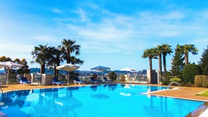 Une piscine d’un bleu éclatant, bordée de chaises longues et d’ombrelles, entourée de palmiers et offrant une vue sur la ville en arrière-plan.