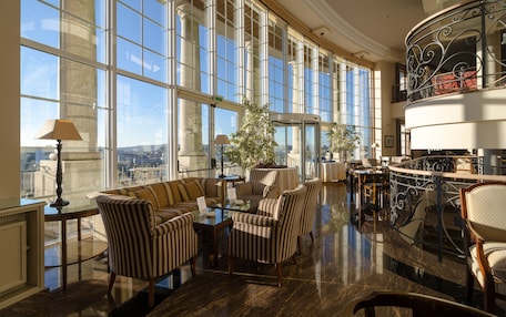 A spacious lobby with large windows, a seating area with striped chairs, a round table, and a decorative railing.