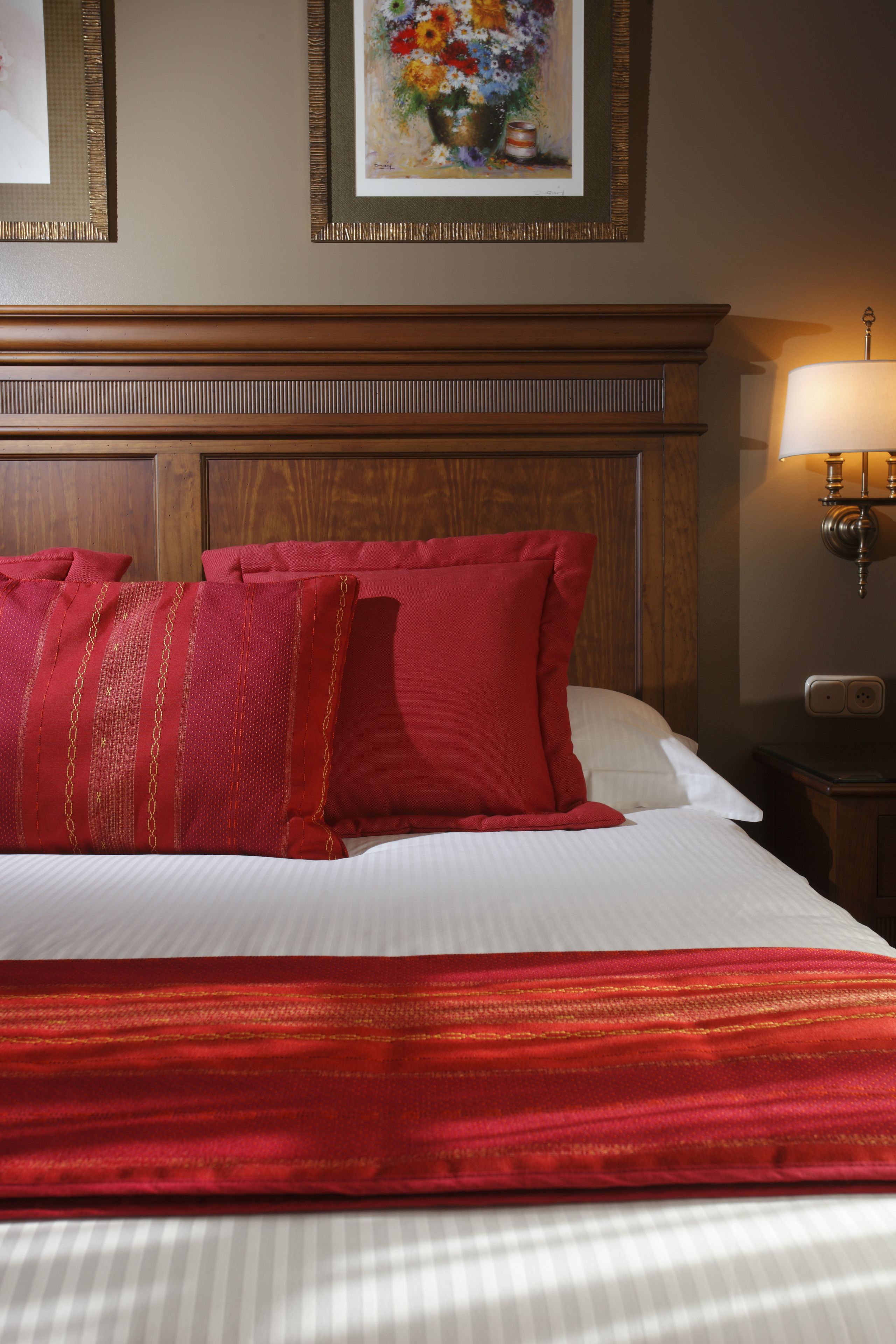 Habitación de hotel con una cama grande, ropa de cama roja y blanca, un cabecero de madera y una obra de arte floral enmarcada en la pared.