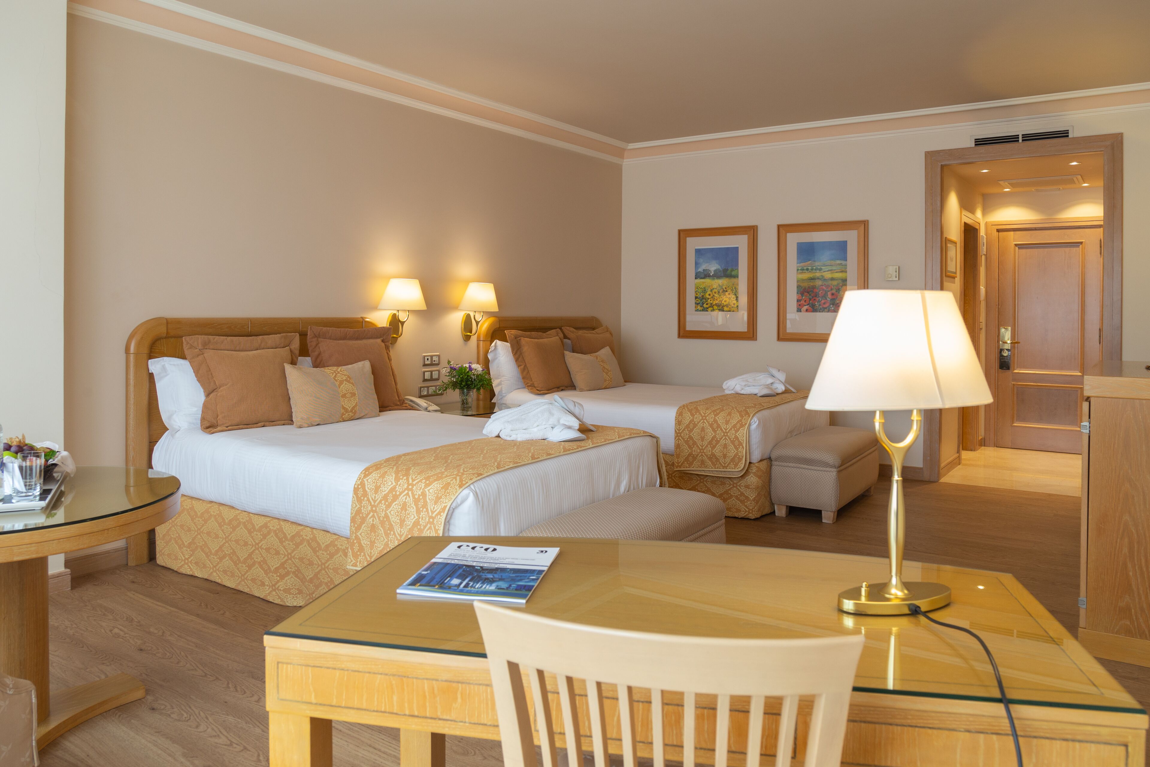 Ein Hotelzimmer mit zwei Betten, einem Schreibtisch, einem Stuhl und einer Lampe.