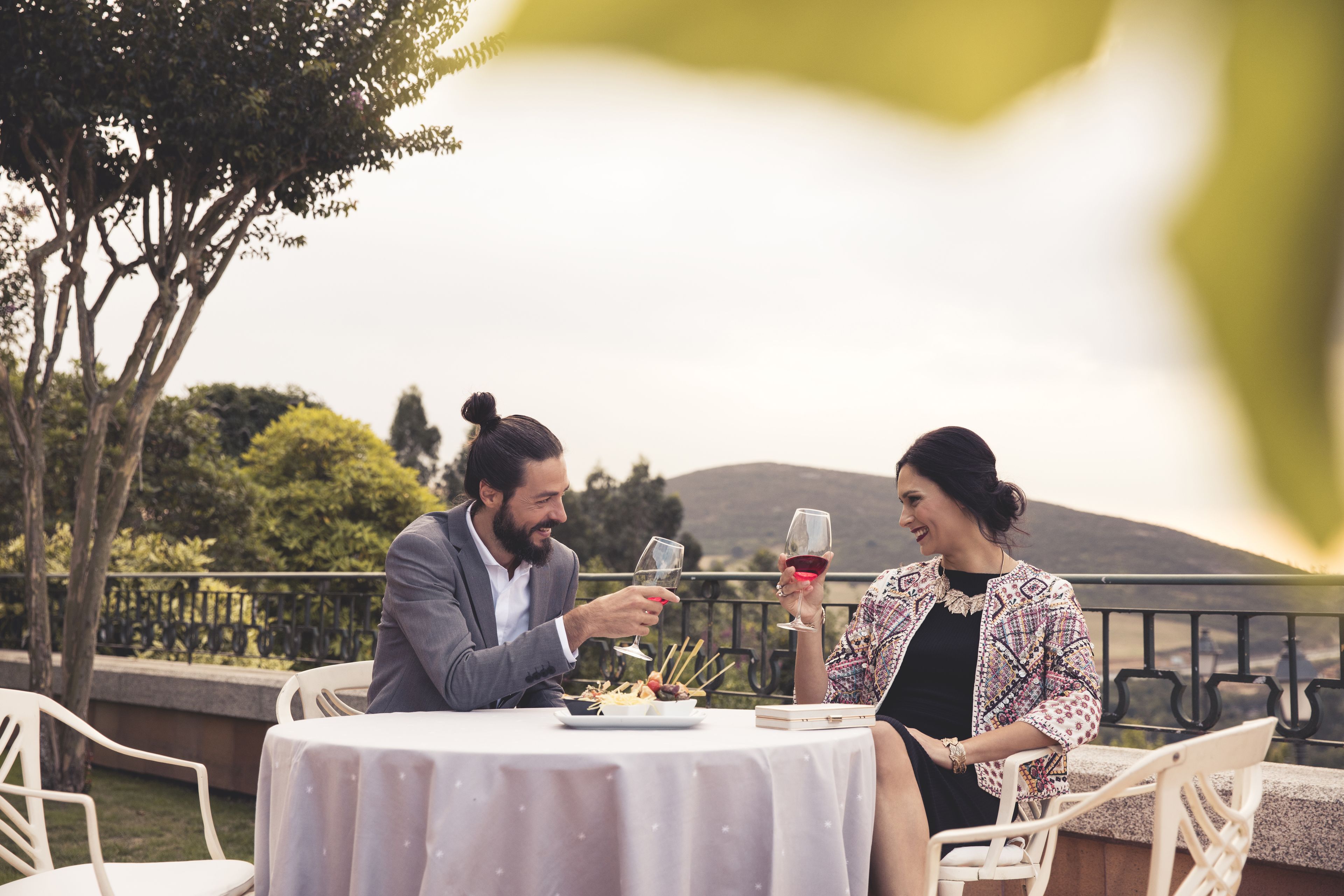 A couple dining outdoors at a table with a view of hills and trees.