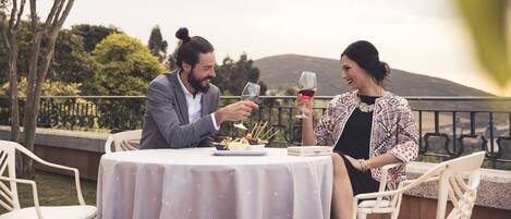 A couple dining outdoors at a table with a view of hills and trees.