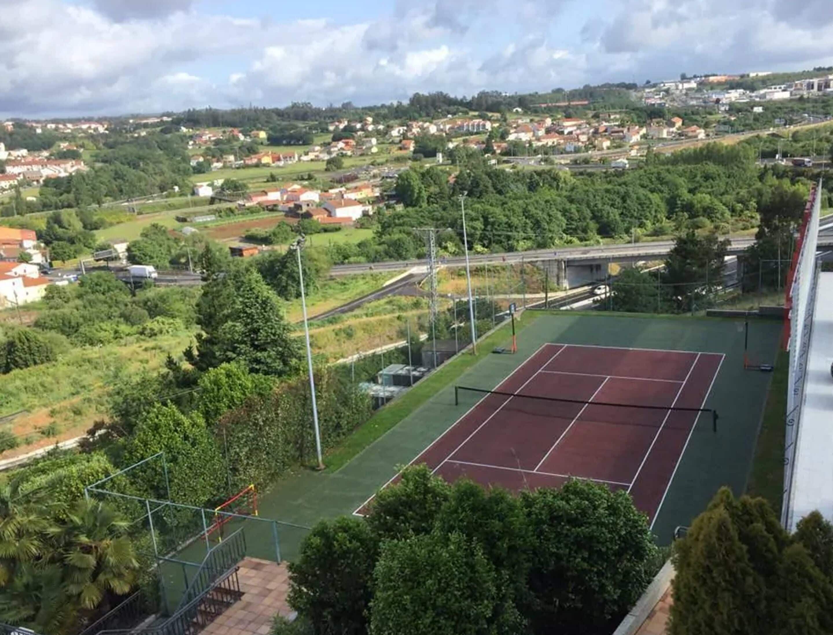 Una cancha de tenis rodeada de áreas verdes y edificios residenciales.