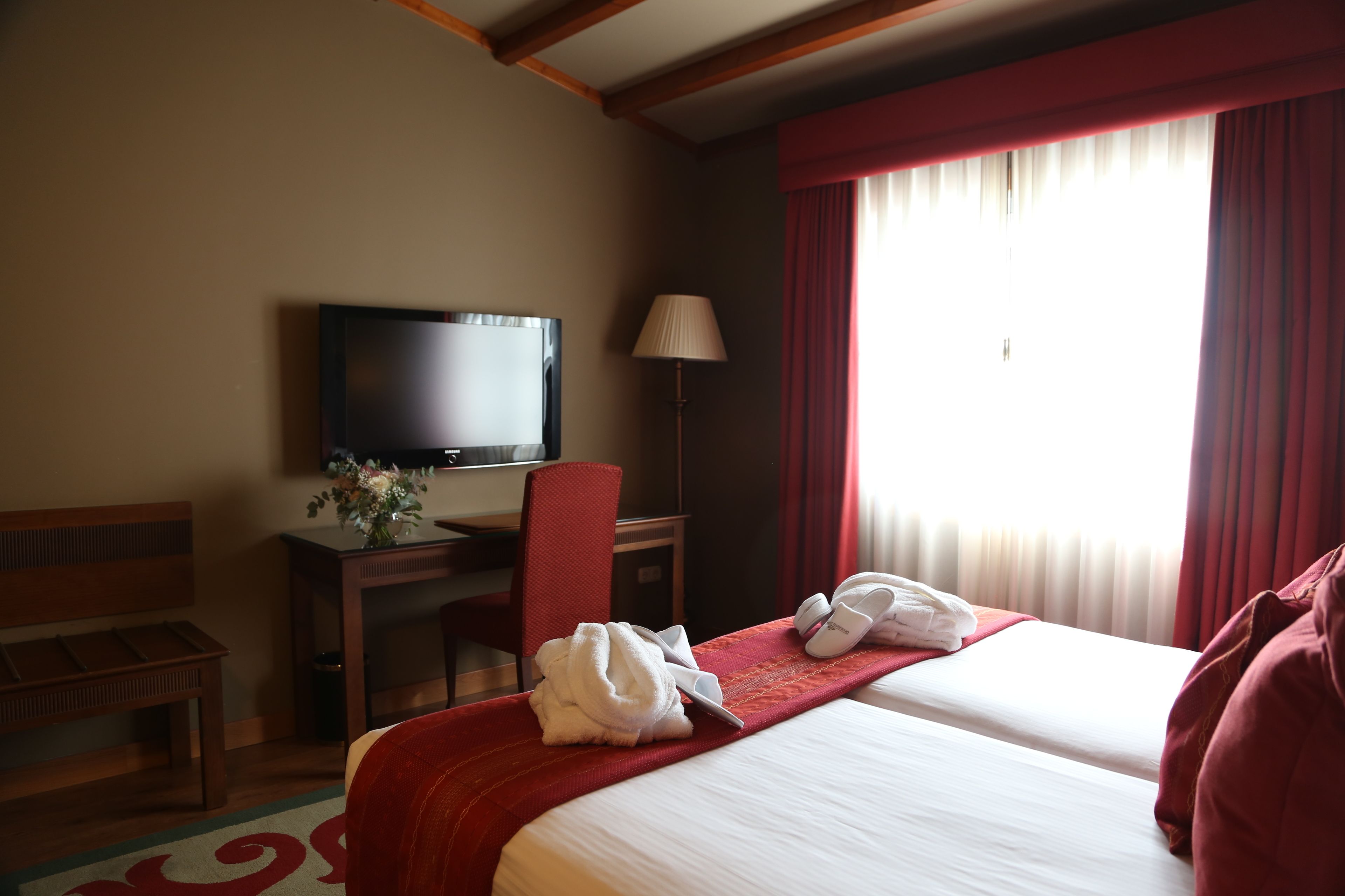 Een hotelkamer met twee bedden, een bureau met een televisie, een stoel en een raam met gordijnen.