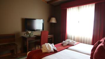 A hotel room with two beds, a desk with a television, a chair, and a window with curtains.