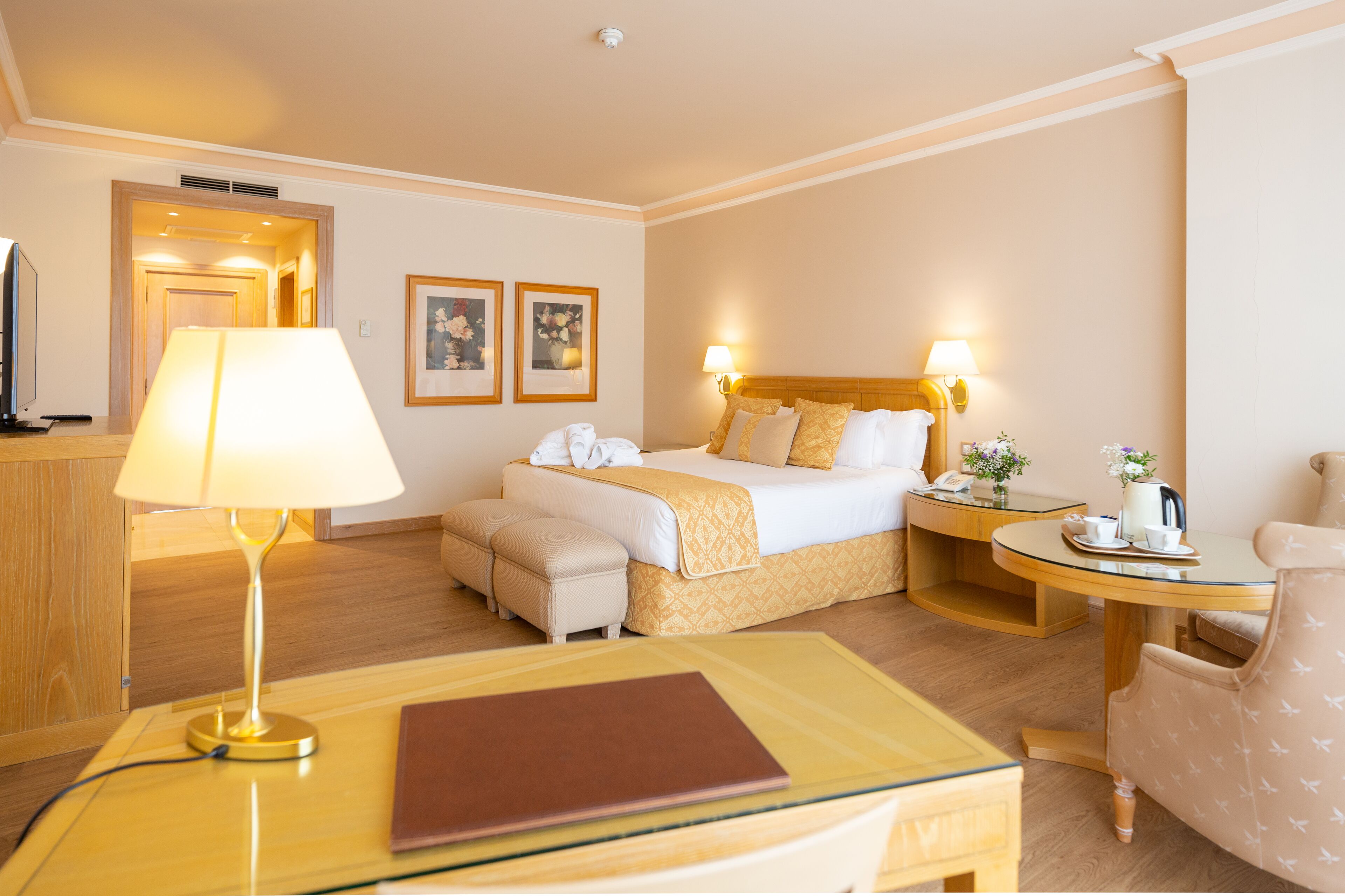 Una habitación de hotel con cama, mesitas de noche, lámpara, silla, escritorio y televisor.