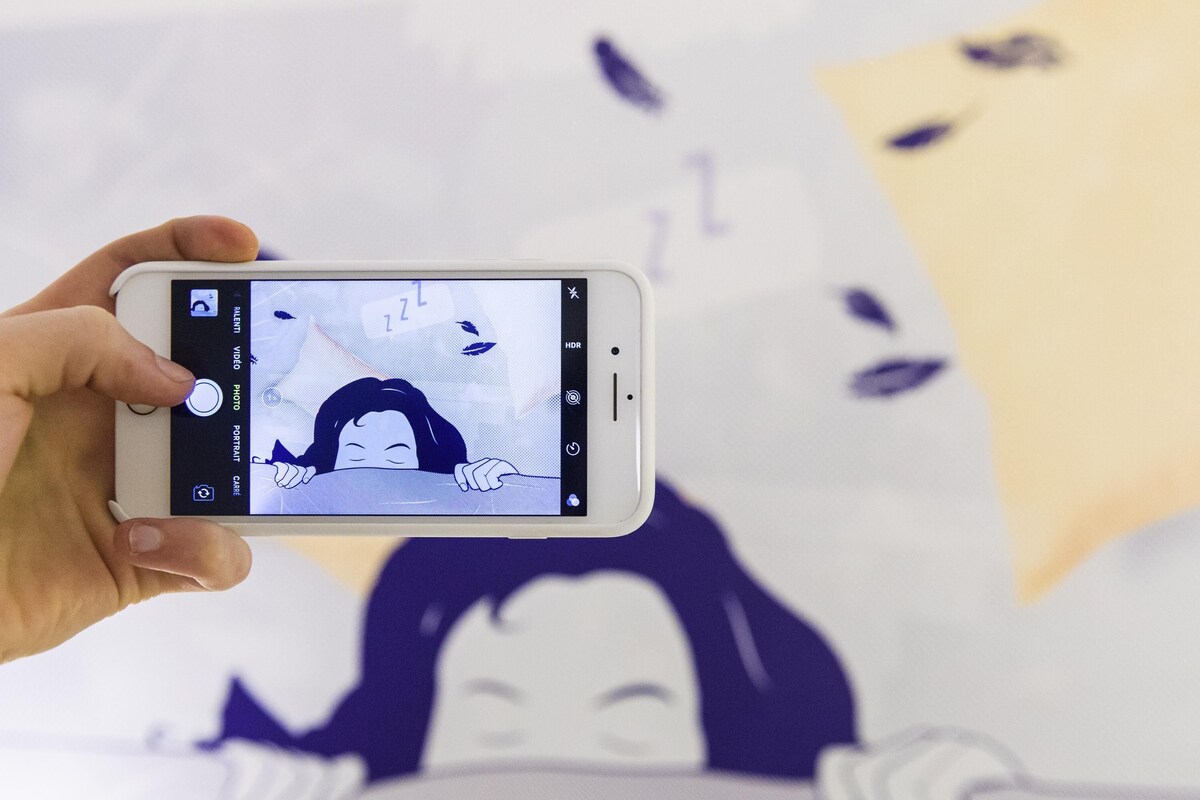 Une main tenant un smartphone sur lequel est affichée une photo d’une personne allongée avec un oreiller.