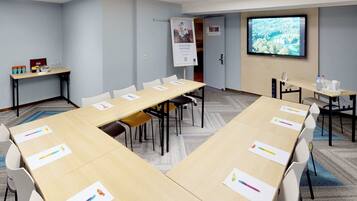 Un salón de conferencias con una larga mesa, sillas blancas, una pantalla de proyector y una pizarra.