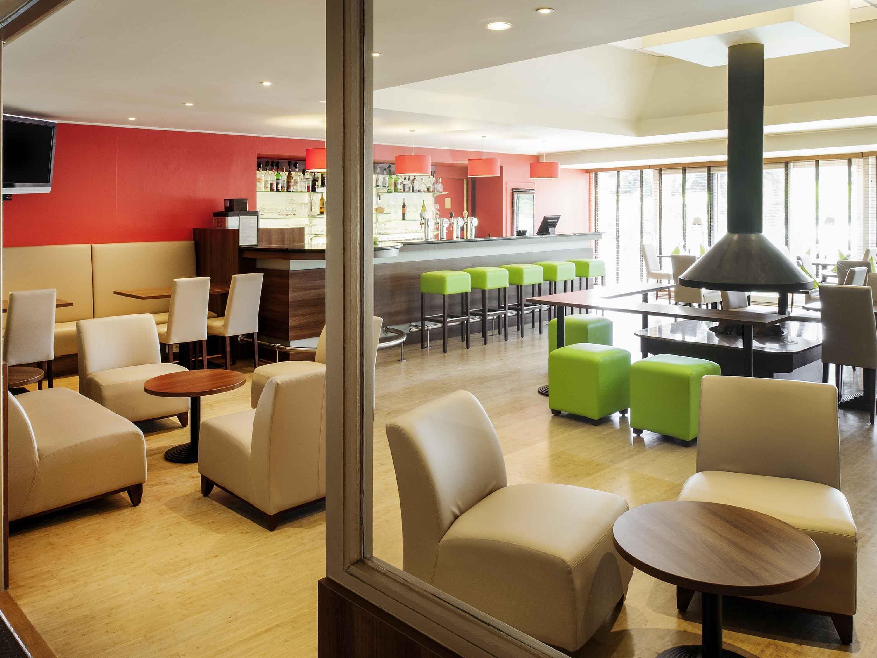 Un moderno hall de hotel con zonas de estar, un bar y un amplio ventanal que proporciona luz natural.