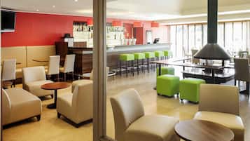Un moderno hall de hotel con zonas de estar, un bar y un amplio ventanal que proporciona luz natural.