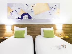 A hotel room with two beds, each with a green pillow, a white headboard, and a wooden wall. There is a painting above the beds, a nightstand with a bottle and glasses, and a pair of headphones on the floor. - ibis Styles Louvain la Neuve Hotel et Events (Ottignies-Louvain-la-Neuve)