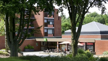 A building with a brick facade, outdoor seating area with tables and chairs, and a covered patio with umbrellas.