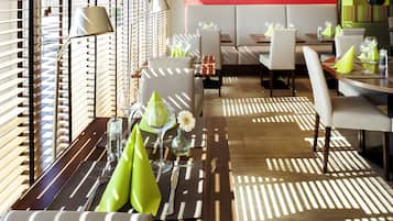 A modern dining area with wooden tables, white cushioned seating, and a bright red accent wall.